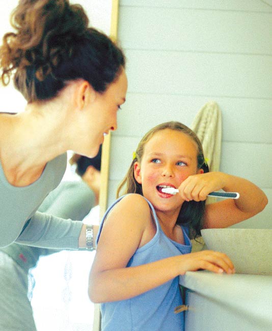 Mother helping daughter brush her teeth