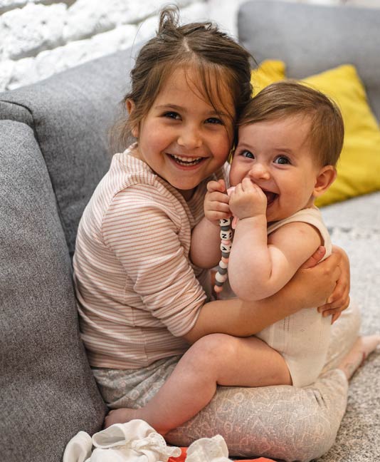 Young girl holding baby that is chewing on beads